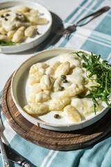 Homemade potato gnocchi with creamy gorgonzola sauce decorated with capers and arugula in white plate on wooden board.