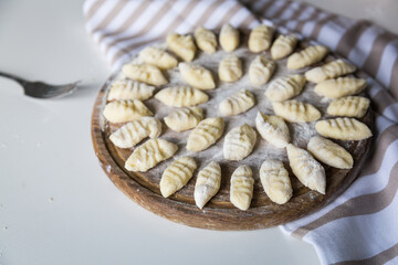 Uncooked homemade potato gnocchi on round wooden board on white background.