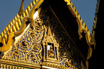 Vue sur un petit Bouddha doré et assis sous un toit, sur une façade du palais impérial à Bangkok. Façade bleue comme le ciel et végétation en spirales dorées.