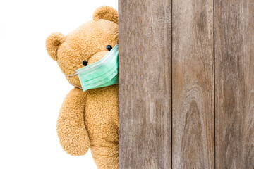 Brown sick teddy bear with protective medical mask behind the old wooden door or window. Stay at home quarantine coronavirus pandemic prevention, covid-19 concept.