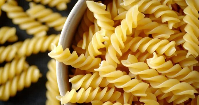 Dry pasta fusilli in plate rotates slowly.