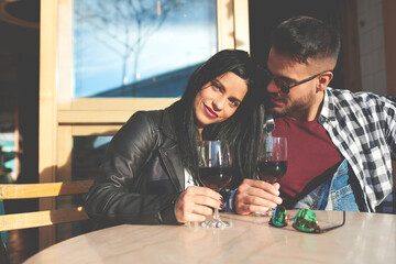 Beautiful happy couple enjoying their honeymoon vacation holidays in Paris. Young female is smiling at the camera while boyfriend looks at her. Boyfriend and girlfriend are sitting in sidewalk cafe