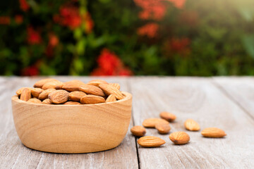 Almond nuts in wooden bowl isolated on  wood table with green nature blurred background. 