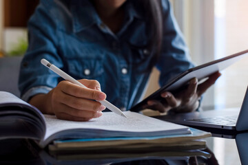 Young woman or female student using digital tablet and work on laptop computer while reading book...