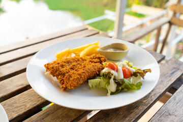 Dish Fish in batter with french fries. Fish on a plate with potatoes and salad in a summer cafe.