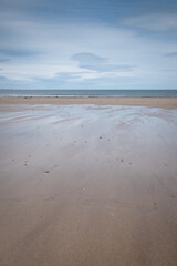 Shimmering, silvery, wet, sandy beach with cloudy, blue sky reflected in water pools below, St Andrews, Fife, Scotland