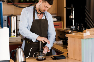Aeropress coffee: barista press to device and coffee drops pours trought aeropress to pot. Alternative coffee brewing method. Handsome bearded barista makes tasty Scandinavian coffee
