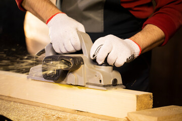 closeup of electric plane throws sawdust while woodworker making wooden detail on workbench at cottage workshop. Carpentry work on wood, wooden chips. Working in country house.