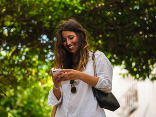 A young caucasian female smiling and using her phone while walking in the street