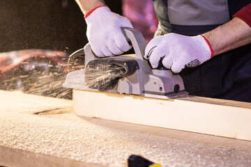closeup of electric plane spitting sawdust while woodworker making wooden detail on workbench at cottage workshop Carpentry work on wood, wooden chips. Working in country house