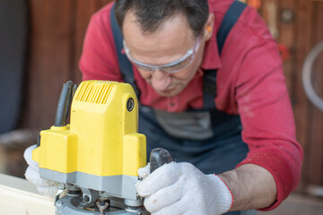 Handsome focused on craftsman processes on wooden workpiece with milling tool close up at cottage workshop. Processing of Wooden beam with milling woodworking machine. Working with hand tool on wood