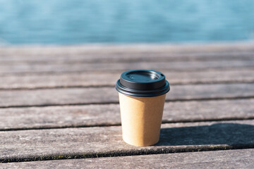 Disposable paper cup of coffee on a wooden background.