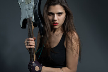 Fototapeta na wymiar beautiful girl holding an electric guitar in her hands, looking at the camera. Studio portrait on a gray background