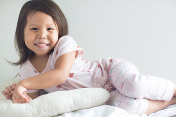 Portrait of cute little asian girl posing and smiling to the camera while laying in bed wearing pajamas.