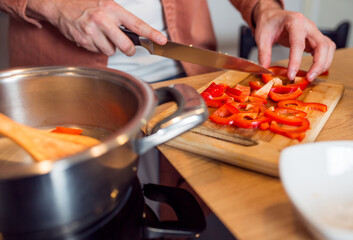Close up of male cutting pepper on wooden board in kitchen