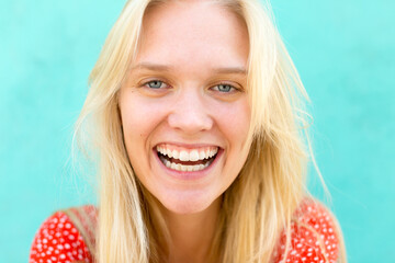Happy beautiful young blonde woman with blue eyes smiling at the camera portrait. Turquoise background. 