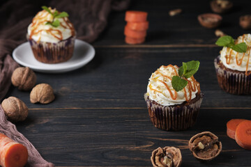 Carrot cupcakes stuffed with caramel and walnuts. Cupcakes with cream cheese cream and icing sugar. The dessert is decorated with mint and caramel.