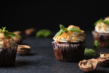 Carrot cupcakes stuffed with caramel and walnuts. Cupcakes with cream cheese cream and icing sugar. The dessert is decorated with mint and caramel.