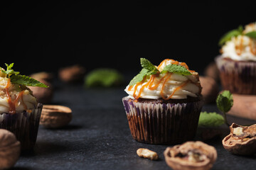 Carrot cupcakes stuffed with caramel and walnuts. Cupcakes with cream cheese cream and icing sugar. The dessert is decorated with mint and caramel.
