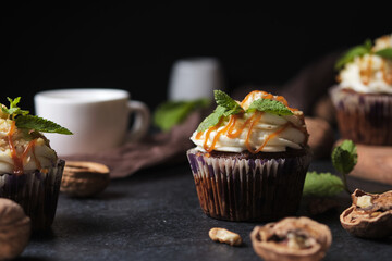 Carrot cupcakes stuffed with caramel and walnuts. Cupcakes with cream cheese cream and icing sugar. The dessert is decorated with mint and caramel.