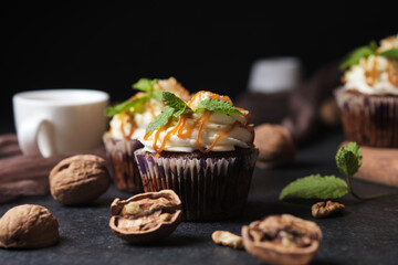 Carrot cupcakes stuffed with caramel and walnuts. Cupcakes with cream cheese cream and icing sugar. The dessert is decorated with mint and caramel.