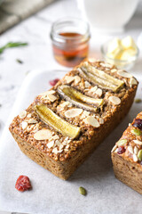 Loaf of Vegan Oatmeal Banana Bread topped with nut, seed, almond slide and banana set on cafe table.