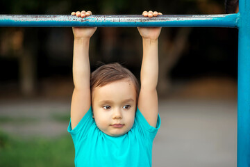 Toddler boy learning to do pull ups at gym lesson in kindergarten: preschooler hanging on worn-out...