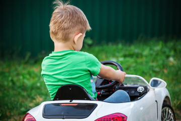 Cute boy in riding a white electric car. Funny boy rides on a toy electric car.