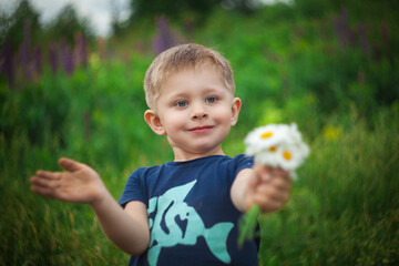 A small boy holds flowers in his hands and smiles.