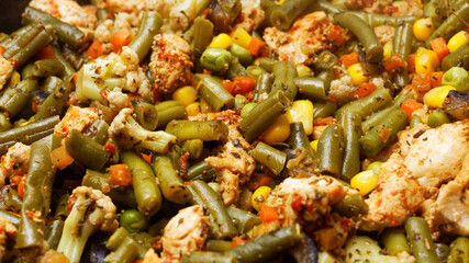 Closeup pieces of chicken meat and vegetables are fried in a pan. Shallow focus.
