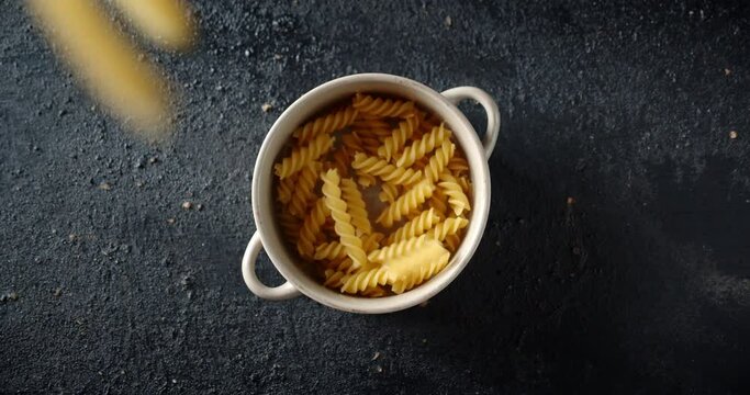 The dry fusilli pasta falling in a bowl on table.