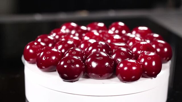 Juicy ripe red cherries rotate clockwise on a white table on a black background. High quality FullHD footage