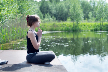Teenage caucasian girl doing yoga exercise on the pond pier