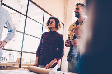 Skilled female member of working team listening to explanation of colleague during informal meeting, young woman thinking over creative ideas of coworkers planning architectural project in office