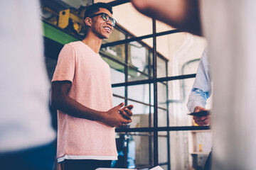 Cheerful afro american guy in eyewear making speech during informal meeting with colleagues, creative young dark-skinned architect explaining his idea of startup project enjoying productive job