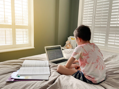 Caucasian boy child sitting in bed and learning online on laptop Internet. Virtual class lesson on video. Self isolation at home. Distant remote video education. A new normal school study for kids.