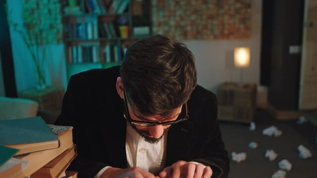 In front of the camera charismatic and expressive man speaking looking straight to the camera in the library he wearing eyeglasses then continue to typing on the typewriter. 4k