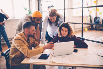 Young crew of developers testing new application on laptop computer discussing opinions and ideas,...