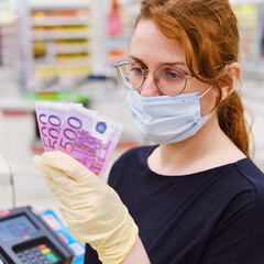 Woman cashier in a medical mask counts money against the background of the cash register. Euros in the hands of the seller in the store