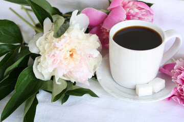 White cup with coffee near peonies on a white background. Close-up. Horizontal photo.