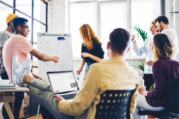 Talented female student explaining to dream team members main concepts of coursework project on board while colleagues communicating with each other and searching useful information in websites