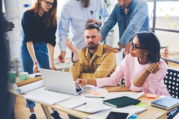 Skilled mature team leader of working group dissatisfied with working process of staff checking architect project via laptop computer, coach explaining solution of problems with startup during meeting