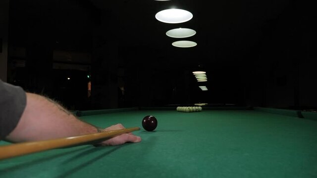 A young man playing Billiards in a club in the evening, he takes aim and prepares to hit the balls with a cue. A young man lines up his shot as he breaks the balls for the start of a game of billiards