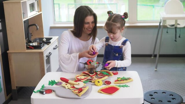 Caucasian girl and boy kid playing and learning at preschool with female teacher. Mother, daughter adn son playing cooking