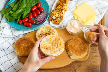 Preparation of all the ingredients for making a burger - bun, cutlet, cheese, salad, tomato, sauces. Top view, girl's hands take a burger roll.