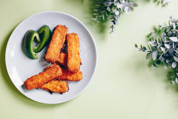 fish sticks in a green plate on an green background and with green plants as decoration.  a few freshly fried fish sticks in a plate that looks tasty