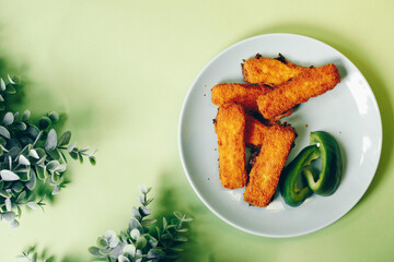 fish sticks with green paprika in a green plate on an green background and with green plants as decoration.  a few freshly fried fish sticks in a plate that looks tasty