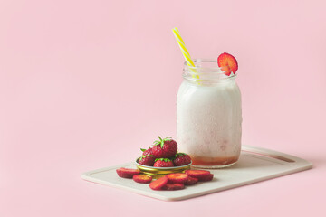 Fresh milkshake in a jar with yellow straws. sliced ripe strawberries on a cutting board