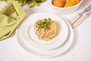 Russian traditional salad Olivier with vegetables and meat in the white plate.