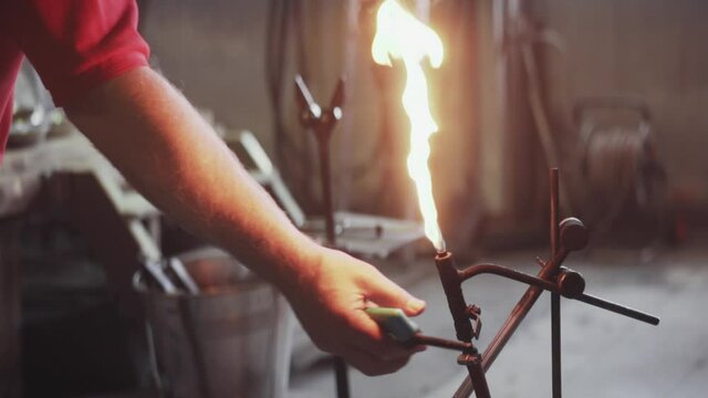 Glass blower artist lights flaming gas torch in workshop - slow motion fire